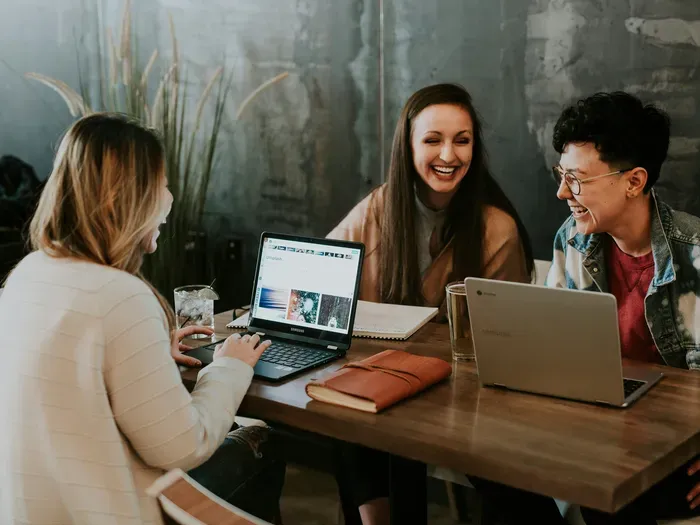 Group of young professionals laughing and collaborating with laptops in a cozy modern cafe setting